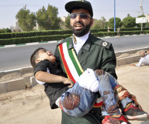 An Iranian carries a wounded boy after a shooting during a military parade. (Behrad Ghasemi/ISNA via AP)
