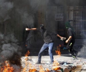 A Palestinian throws a stone toward an Israeli soldier during clashes in Hebron, Friday, Sept. 27, 2013, on the 13th anniversary of the second Palestinian "Intifada," or uprising.
