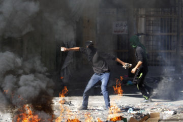A Palestinian throws a stone toward an Israeli soldier during clashes in Hebron, Friday, Sept. 27, 2013, on the 13th anniversary of the second Palestinian "Intifada," or uprising.