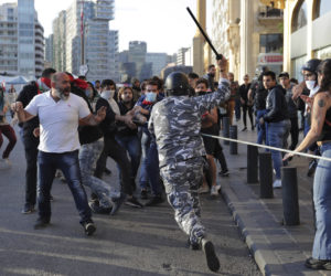 A police officer raises his baton to anti-government protesters during clashes during a protest in downtown Beirut, Lebanon, Nov. 19, 2019.