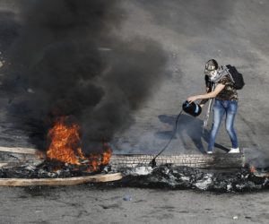 An anti-government protester drops oil on burning tires and wood during ongoing protests after weeks of calm in Beirut, Lebanon, Tuesday, Jan. 14, 2020.
