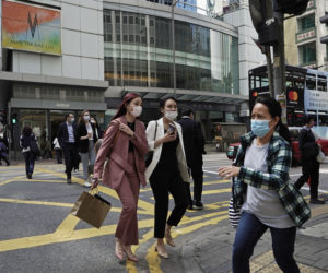 People wearing masks, walk across a street in Hong Kong, Monday, Feb. 24, 2020.