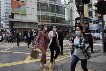 People wearing masks, walk across a street in Hong Kong, Monday, Feb. 24, 2020.