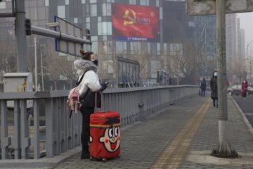 A traveler stands on a bridge near a display showing government propaganda in the fight against the COVID-19 viral illness in Beijing, China Thursday, Feb. 13, 2020.