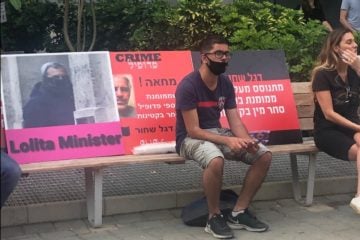 A protester sits in front of former PM Ehud Barak's Tel Aviv residence, with signs linking him to pedophile financier Jeffrey Epstein. (Lauren Marcus)