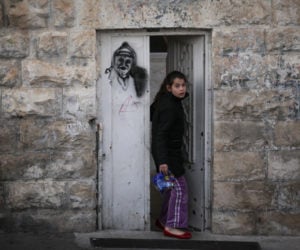 An east Jerusalem girl walks out her front door, which has a grafitti image of the late former Palestinian Authority leader, Yasser Arafat, in the village of Ras Al-Amoud, near the Mount of Olives, on January 29, 2014. (Flash90/Hadas Parush)