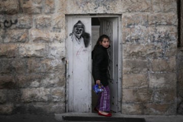 An east Jerusalem girl walks out her front door, which has a grafitti image of the late former Palestinian Authority leader, Yasser Arafat, in the village of Ras Al-Amoud, near the Mount of Olives, on January 29, 2014. (Flash90/Hadas Parush)