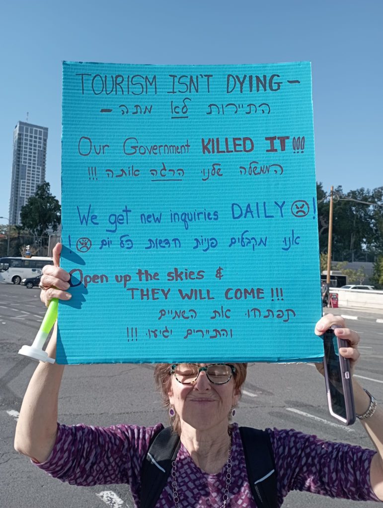 A tour guide holds up a sign blaming the Israeli government for the prolonged shutdown of the tourism industry. Tel Aviv, Dec 27, 2021. Photo: Josh Levinson